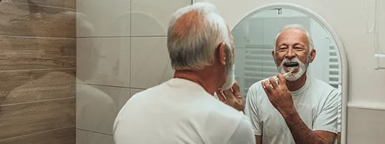 senior man looking into a mirror while brushing his teeth