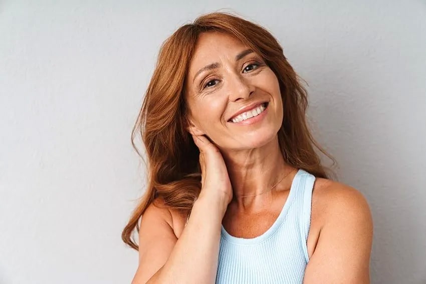 Mature red haired woman places her hand behind her neck and smiles