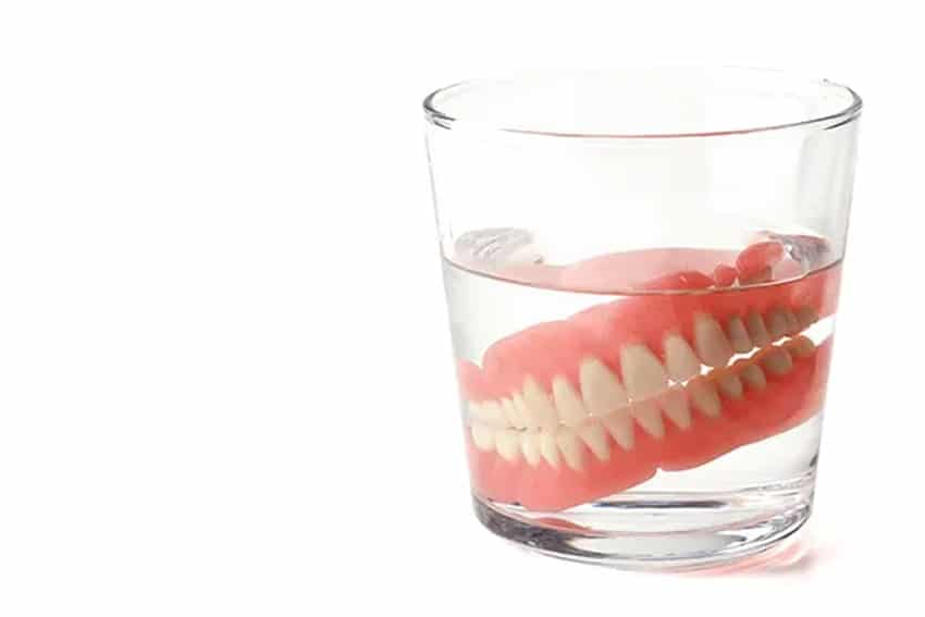 A set of traditional dentures sitting in a glass of water, soaking