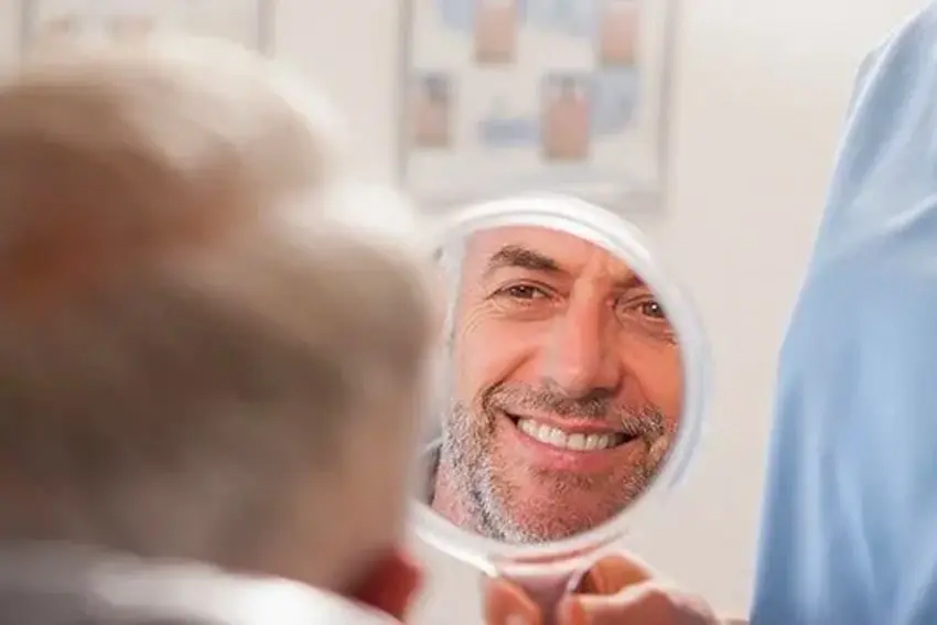 Older man looking in a handheld mirror at the dentist office