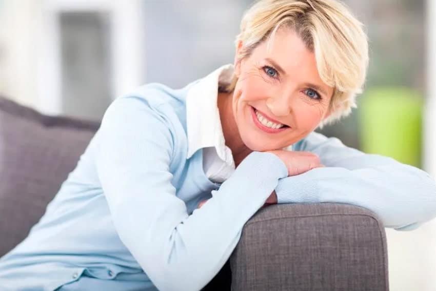 Attractive older woman relaxes on her gray couch